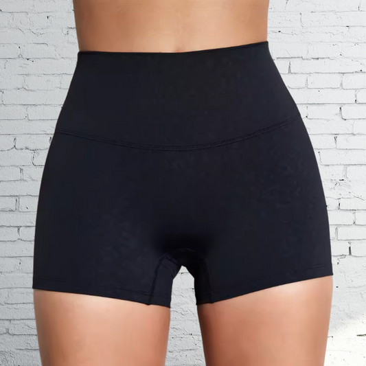 Black high-waisted shorts worn by a person against a white brick wall background